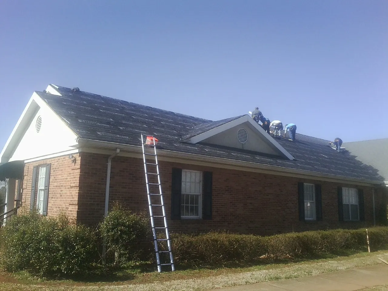 Crew tearing shingles off a brick ranch roof with a ladder set — Emergency Roof Repair work by our crew in Landing