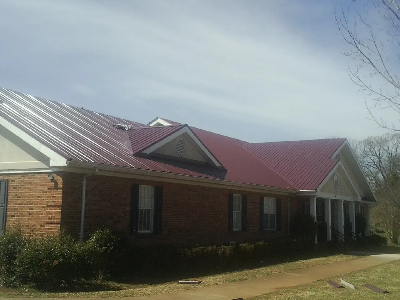 Red metal roof with gabled entries on a long brick building, from a Hail Damage Roof Repair job in Landing