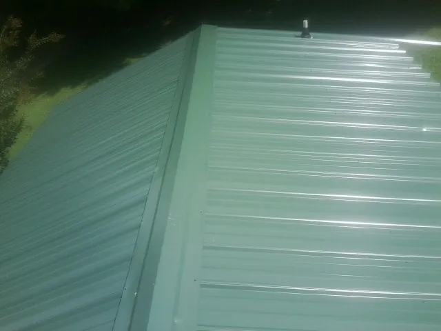 New green metal panels meeting at the ridge of a roof — Flat Roof Repair work by our crew in Landing