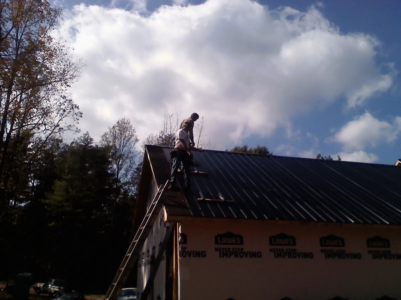 Roofer fastening dark metal panels high against a cloudy sky, from a Roof Inspection job in Landing