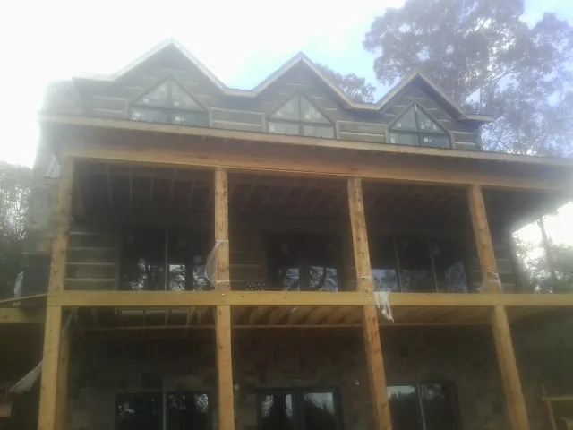 Dormers and porch framing on a large log home under construction — Roof Coating work by our crew in Landing